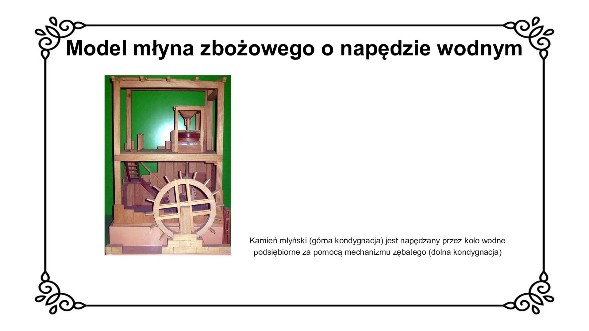 Biały slajd. U góry nagłówek: „Model młyna zbożowego o napędzie wodnym”. Niżej, po lewej stronie slajdu, zdjęcie przedstawiające wykonany z drewna schemat działania młyna zbożowego o napędzie wodnym. Pokazano dwie kondygnacje młyna. W górnej znajduje się kamień młyński, a w dolnej koło wodne podsiębiorne. Wejście do młyna po schodach znajduje się na poziomie pierwszego piętra. Obok zdjęcia, z prawej strony slajdu, tekst: „Model młyna zbożowego o napędzie wodnym. Kamień młyński (górna kondygnacja) jest napędzany przez koło wodne podsiębiorne za pomocą mechanizmu zębatego (dolna kondygnacja)”.