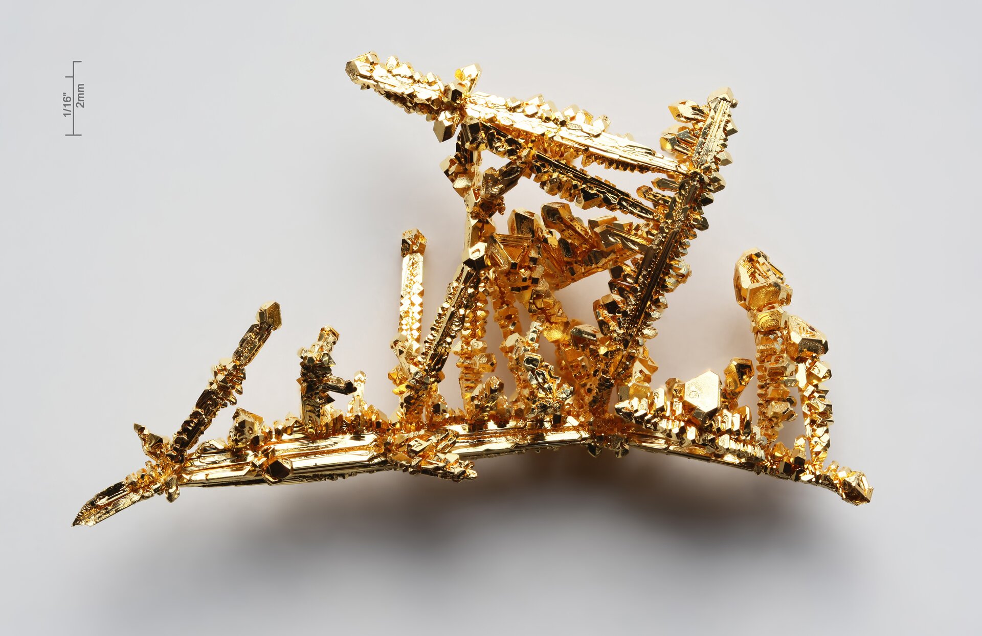 Zdjęcie przedstawia kawałek złota. Przypomina kształtem delikatną gałązkę.  Ma złoty kolor i wyraźny połysk. Kryształy są nieregularnie pozrastane.