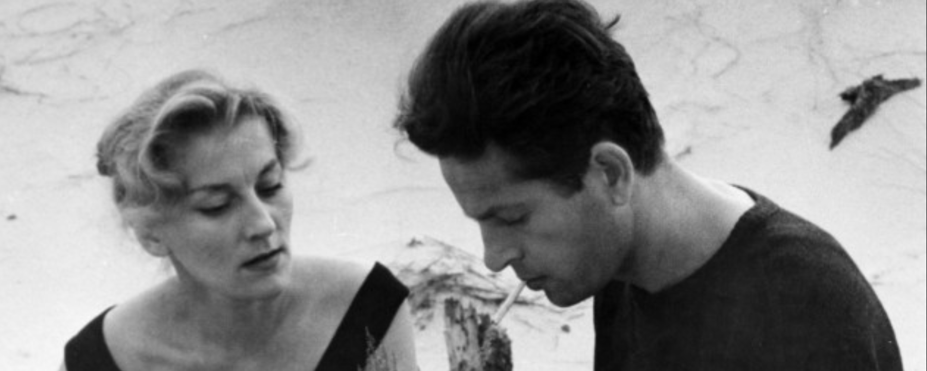 Zdjęcie przedstawia parę dojrzałych ludzi - kobietę i mężczyznę. Kobieta patrzy na mężczyznę, a on ma spuszczony wzrok. W ustach ma zapalony papieros.