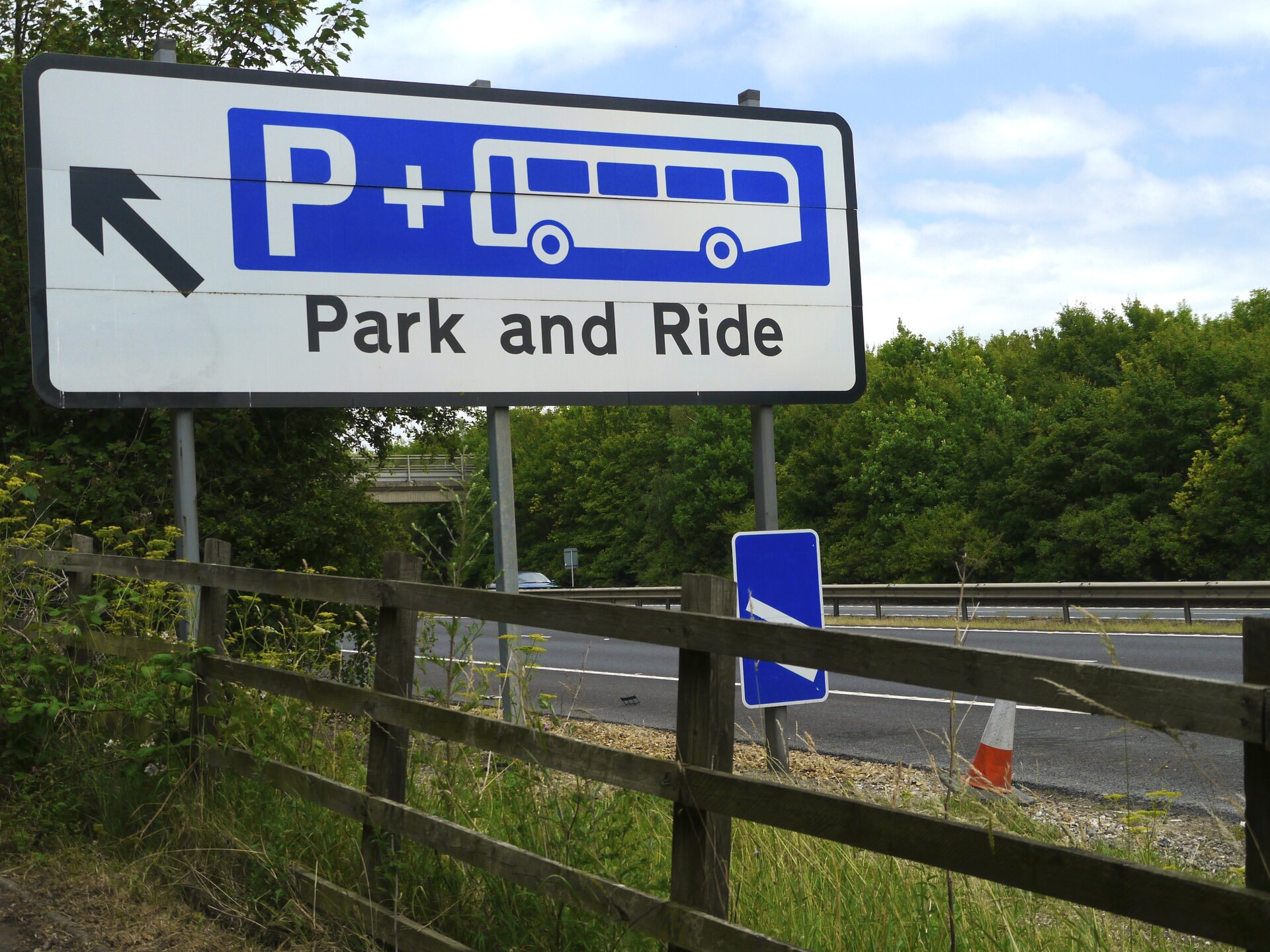 Na zdjęciu znak drogowy. Napis zaparkuj i pojedź. Litera pe i autobus. W tle droga i las.