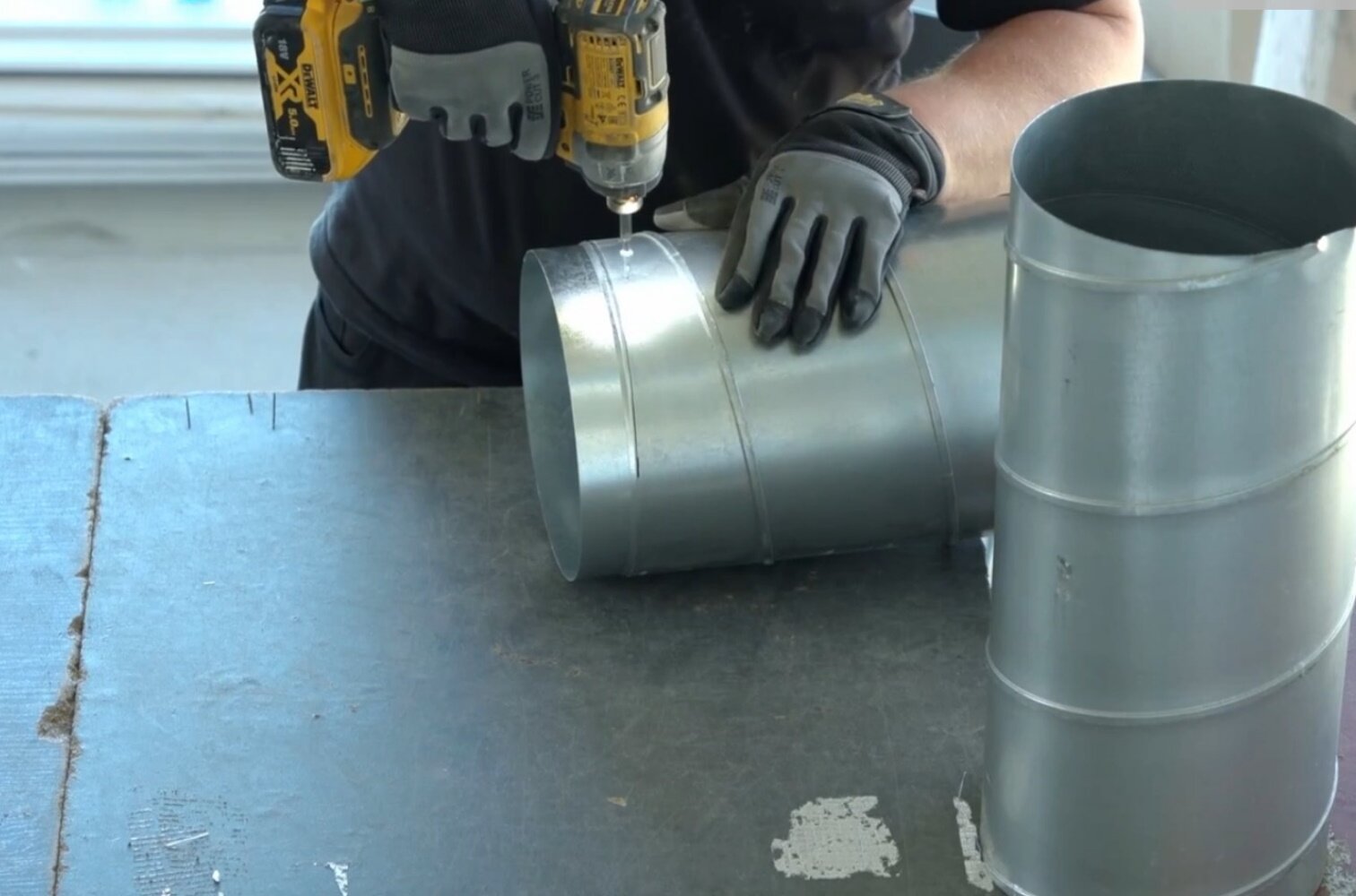 Zdjęcie przedstawia łączenie rur typu spiro za pomocą nypla i wkrętów samogwintujących. Pracownik w stroju roboczym za pomocą wkrętarki wykonuje wymienioną czynność.
Opisy prezentowanych na grafikach obiektów są załączone w treści.