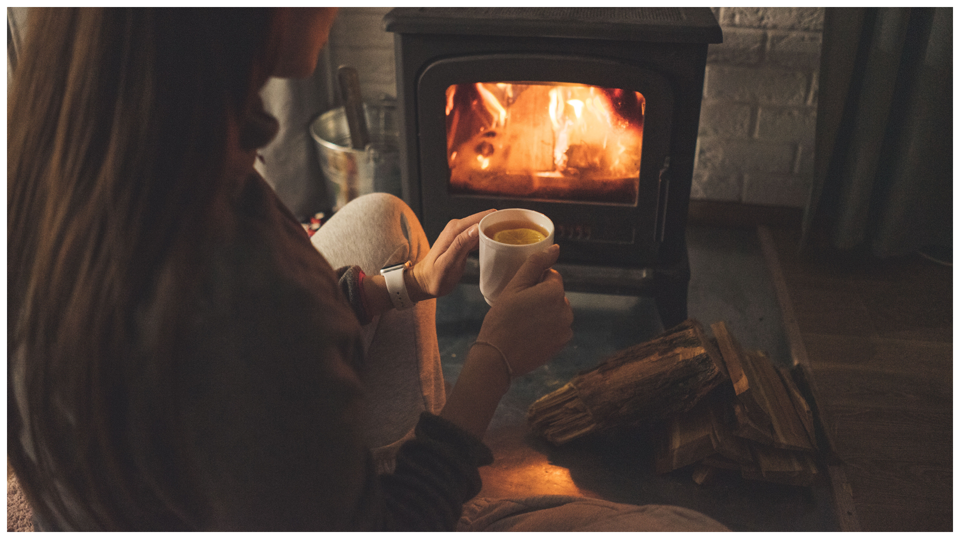 Zdjęcie kobiety, która siedzi przy kominku z kubkiem herbaty z cytryną.