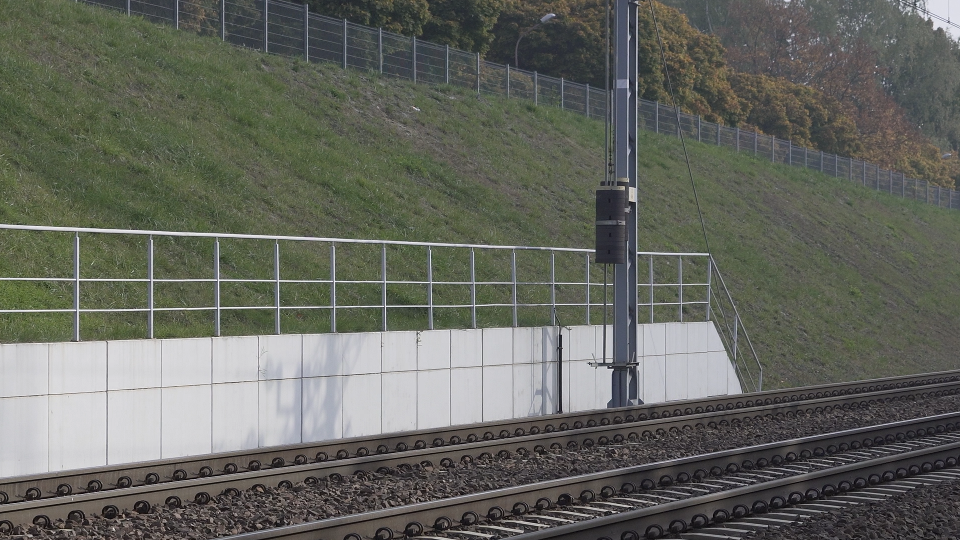  Zdjęcie przedstawia nowoczesny mur oporowy przed tunelem kolejowym. Mur wykonany jest z prefabrykowanych płyt połączonych ze sobą. Na szczycie muru znajduje się balustrada.