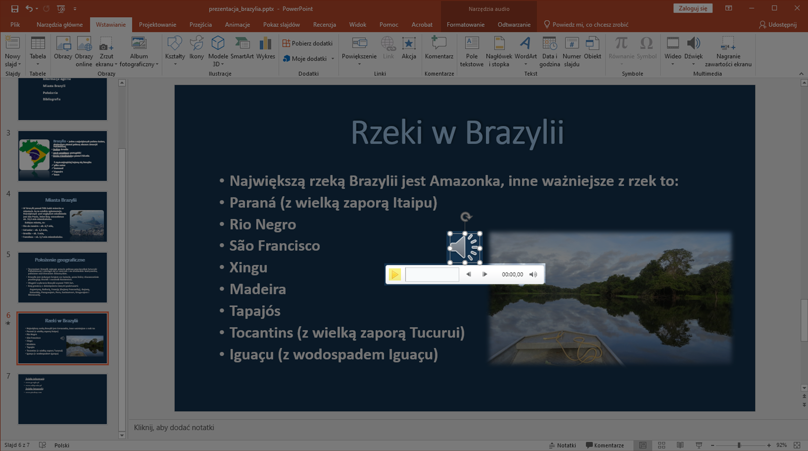 Zrzut ekranu przedstawia wycinek okna programu Microsoft PowerPoint. Prezentacja zapisana jest jako prezentacja brazylia.pttx. W programie znajdują się zakładki takie jak „Plik”, „Narzędzie główne”, „Wstawianie”, „Projektowanie”, „Przejścia”, Animacje”, „Pokaz slajdów”. Recenzje”, „Widok”, „Pomoc”, „Acrobat” , "Formatowanie", "Odtwarzanie" oraz „Powiedz mi, co chcesz zrobić”.  Po lewej stronie znajduje się lista slajdów. Prezentacja składa się aktualnie z siedmiu slajdów. Wybrano slajd szósty. Na większości okna programu znajduje się powiększony slajd szósty o nazwie Rzeki w Brazylii. Na slajdzie zapisano nazwy rzek w Brazylii. Pod slajdem znajduje się miejsce na notatkę. Całe okno prezentacji jest wyciemnione. Na środku slajdu pojawia się ikonka głośnika.  Po kliknięciu w głośnik pojawia się pasek z przyciskiem plej, prostokątem wskazującym czas trwania utworu, przyciskiem ze strzałką w lewo, przyciskiem ze strzałką w prawo, zegarem oraz przycisk z głośnikiem do regulacji głośności. 