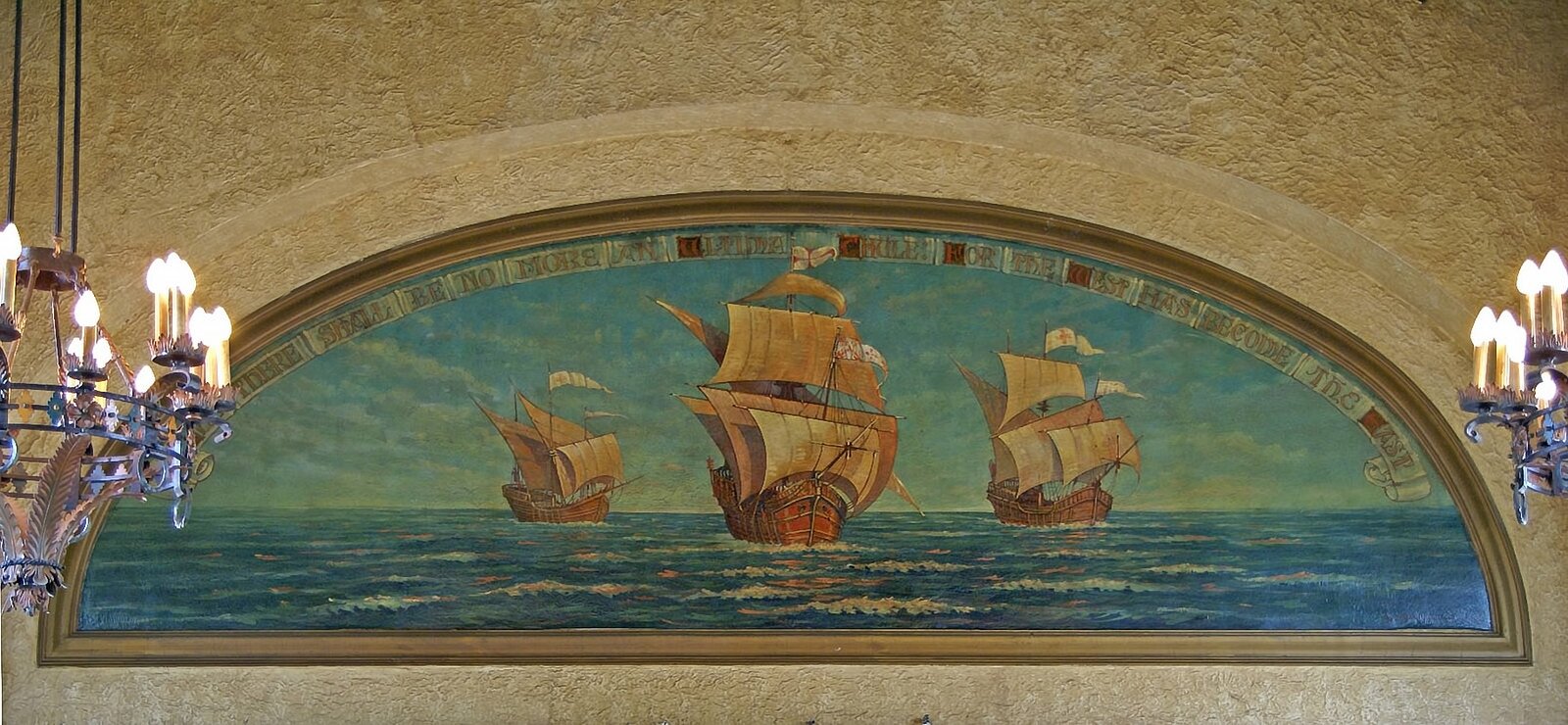 Malowidło umieszczone w ścianie budynku prezentujące trzy karawele na otwartym morzu. Drewniane okręty mają rozwinięte duże żagle, na morzu dookoła nich lekkie fale.