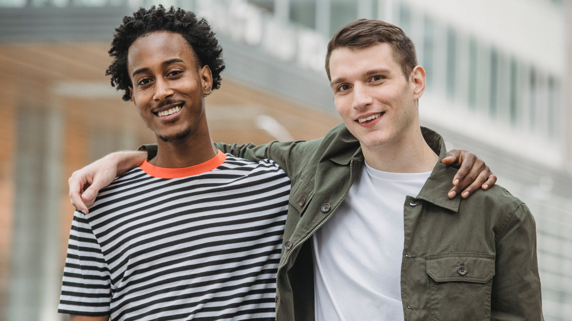 Zdjęcie przedstawia dwóch szczupłych, wysokich chłopaków. Chłopak po lewej stronie  ma ciemną skórę, po prawej białą. Są radośni, uśmiechają się.