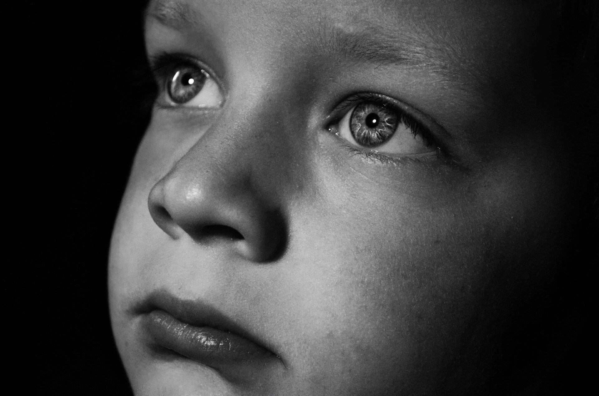 Smutna, zatroskana twarz małego chłopca z oczami patrzącymi w dal, na czarnym tle.