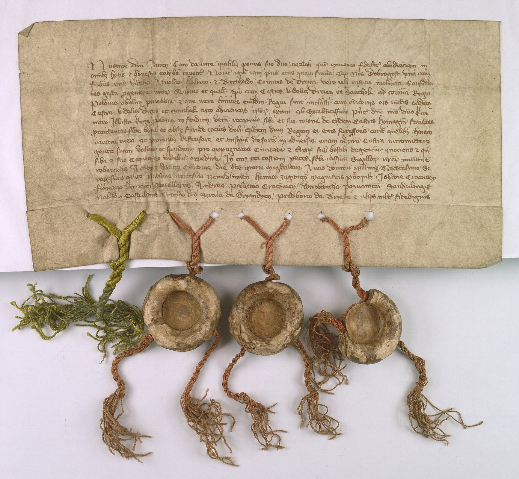 Ilustracja przedstawia oryginalny średniowieczny dokument. Został on sporządzony na pergaminie. Treść wypisano pismem odręcznym. Do dokumentu przyczepione są trzy pieczęcie lakowe.