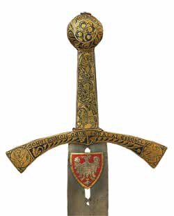 Zdjęcie przedstawia miecz Szczerbiec. Rękojeść jest złota oraz ozdobiona liściastymi motywami. Pod nią już na ostrzu znajduje się herb z białym orłem na czerwonym tle.