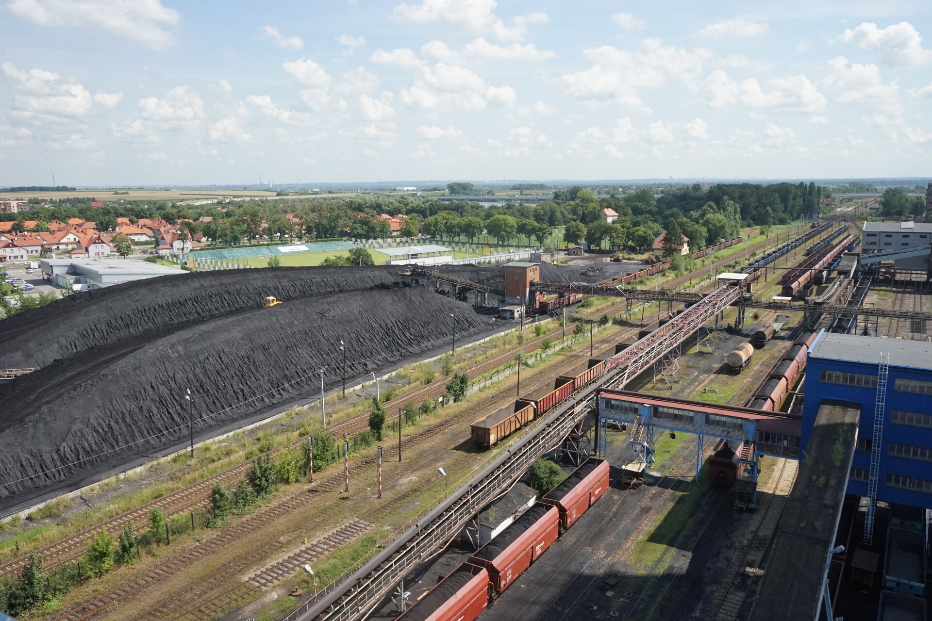 Na zdjęciu widać zwały węgla. Węgiel jest składowany w formie pryzmy. Widoczny węgiel ma małe rozmiary ziarna. Obok zwałów widoczne są bocznice kolejowe ze stającymi na torach wagonami załadowanymi węglem. Poniżej zdjęcia widoczny jest przycisk multimedialny z nagraniem audio. Treść nagrania jest zgodna z tytułem zdjęcia.