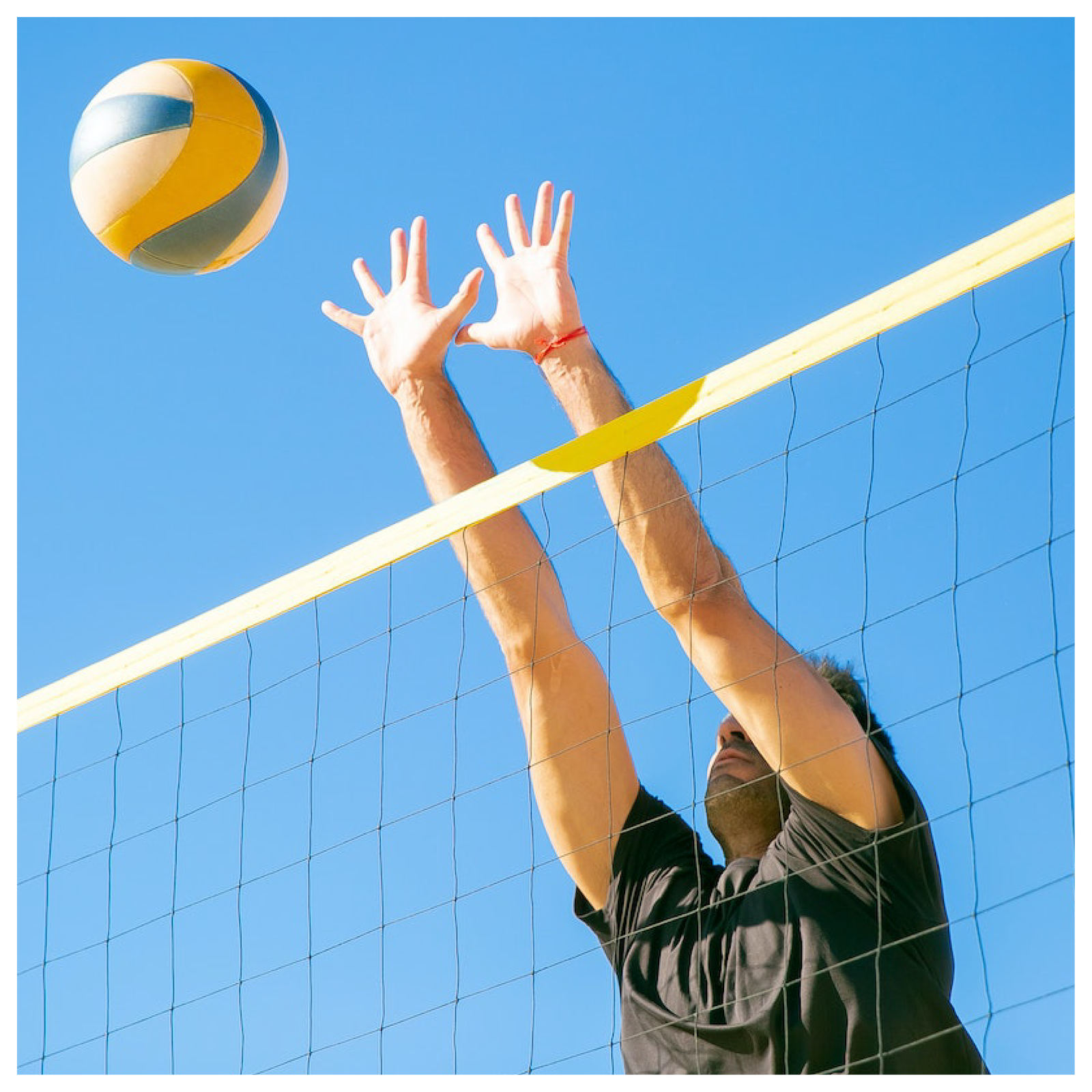 Obrazek przedstawia mężczyznę z wyciągniętymi do góry rękami ku piłce znajdującej się ponad siatką do siatkówki.