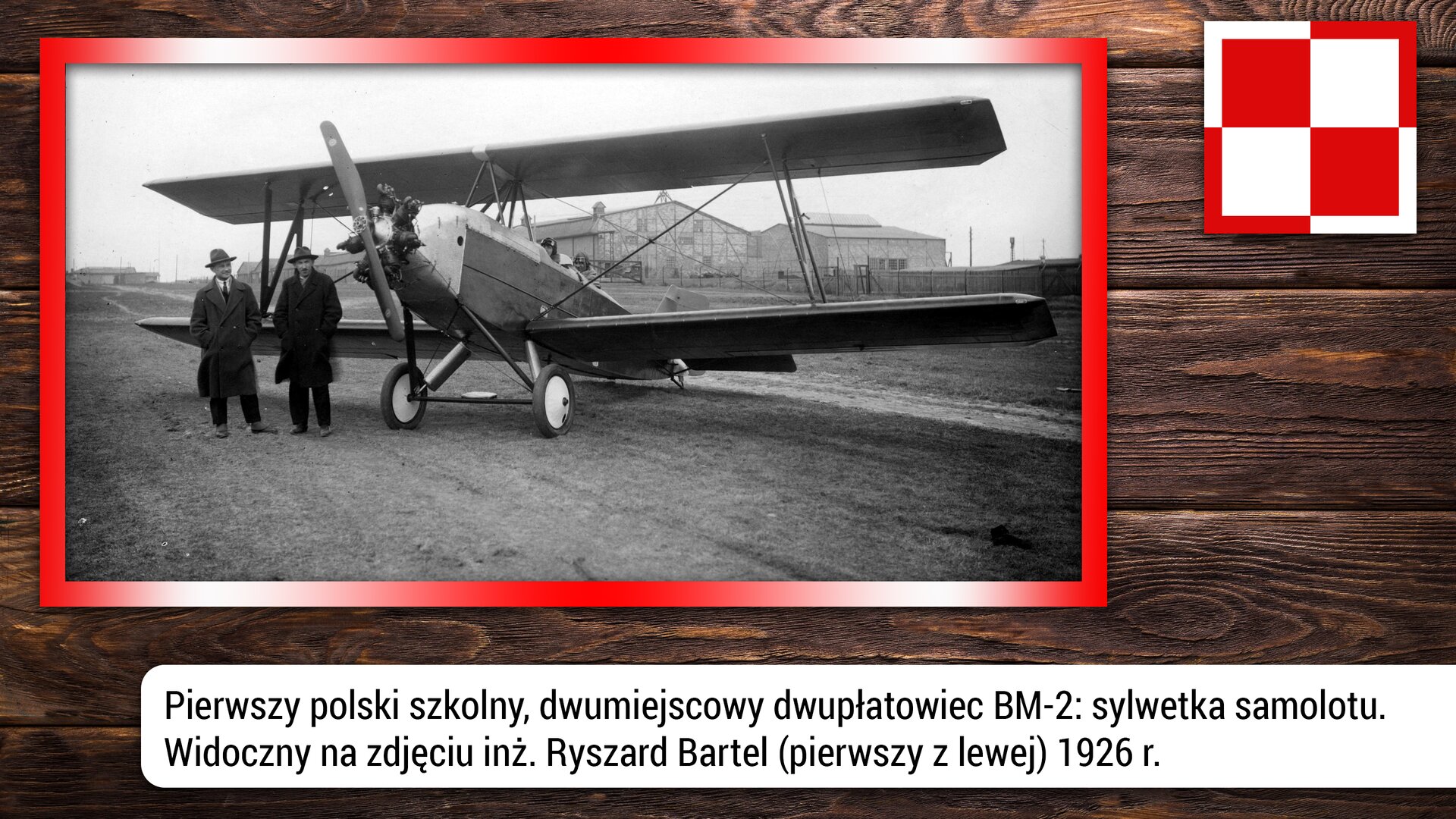Fotografia przedstawia pierwszy polski, szkolny, dwumiejscowy samolot dwupłatowiec MB-2. Na zdjęciu szczególnie widoczne są dwa płaty, korpus i śmigło. Dwupłatowiec był popularnym typem samolotu na początku dwudziestego wieku. Dwupłatowiec wyróżnia się swoją konstrukcją, ponieważ składa się z dwóch płatów nośnych, czyli dwóch „skrzydeł” umieszczonych jedno pod drugim. Po lewej stronie zdjęcia, przy samolocie stoją dwie postaci. Po lewej stoi Ryszard Bartel – to polski inżynier, konstruktor lotniczy i pilot. Zdjęcie zrobiono w 1926 r.