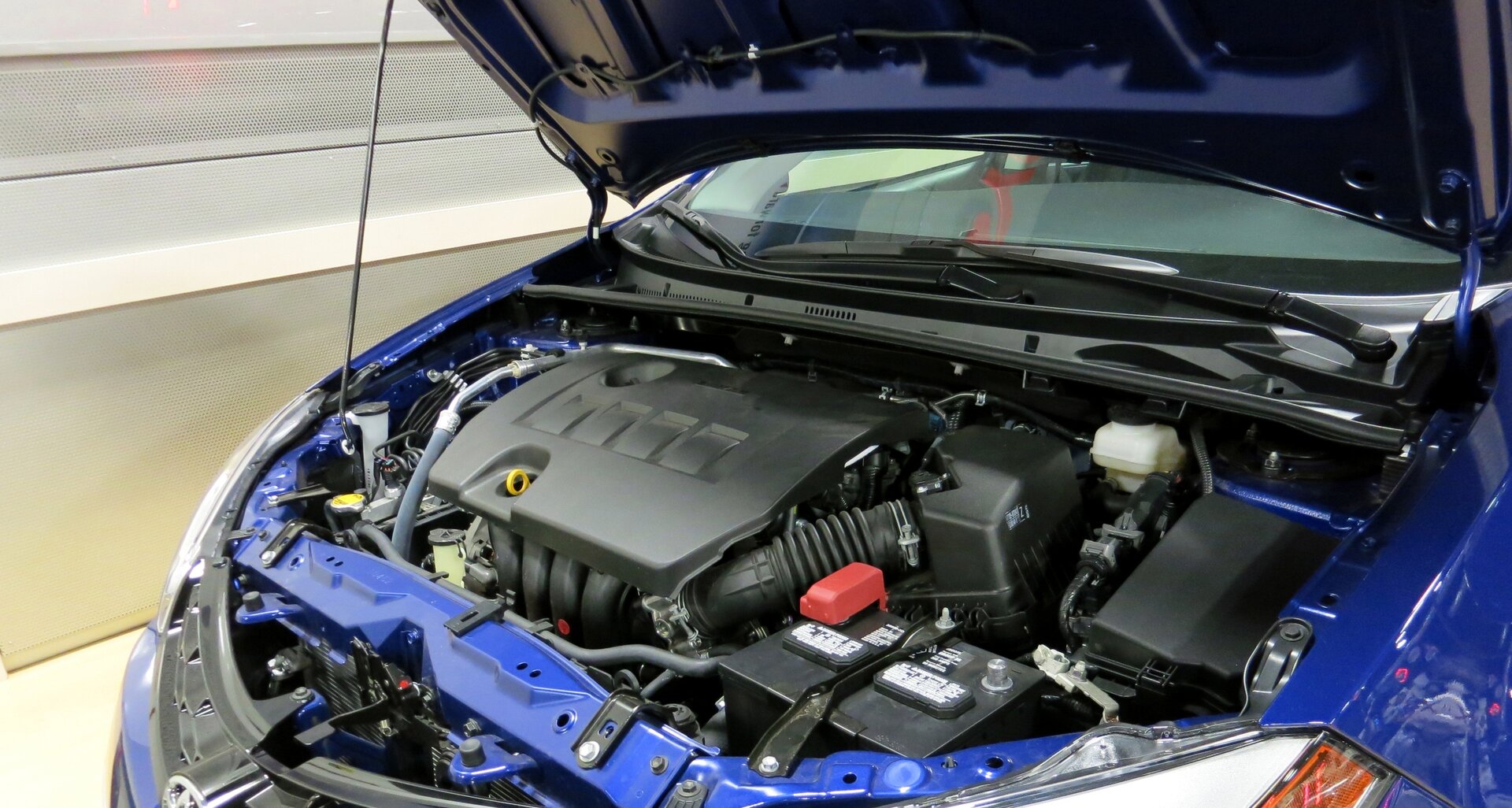 Zdjęcie przedstawia silnik i inne elementy niebieskiego samochodu widoczne po otwarciu maski.