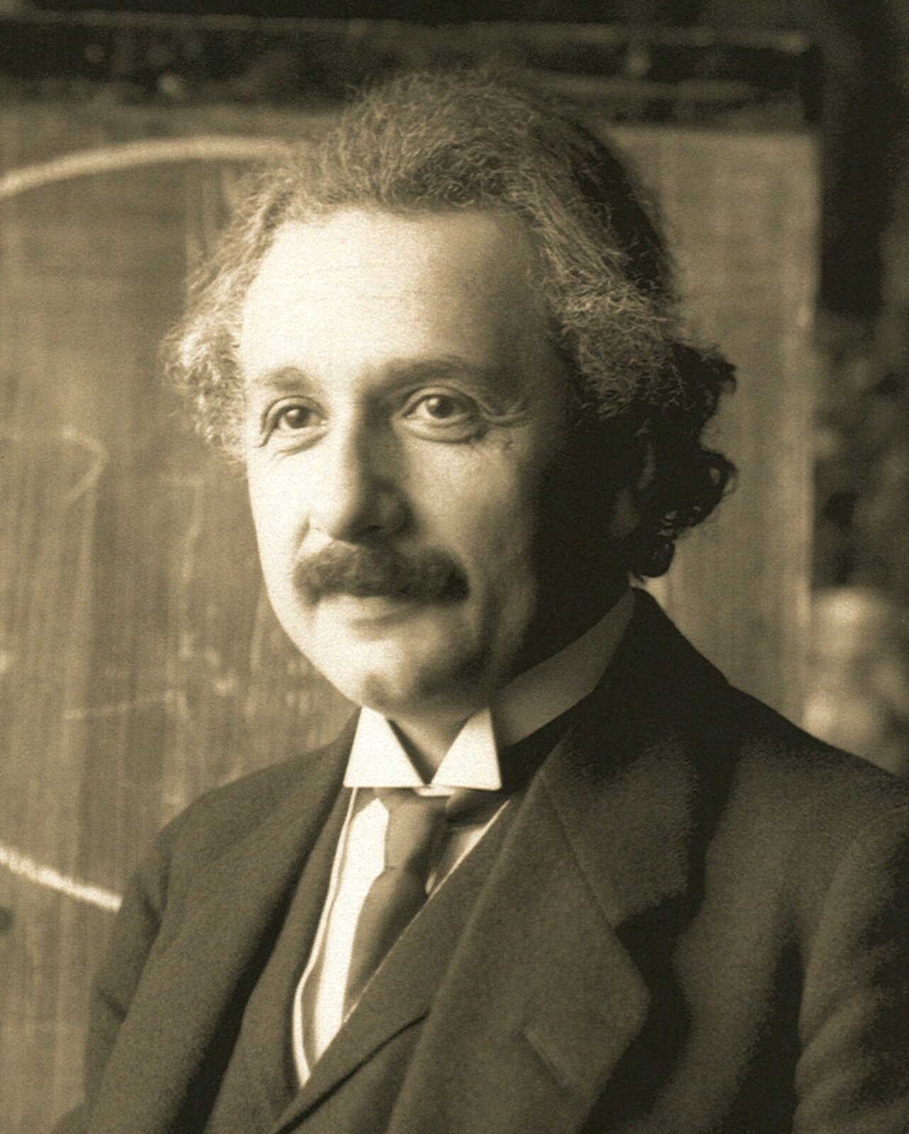 Rys. 3. Zdjęcie poglądowe przedstawia portret Alberta Einsteina. To uśmiechnięty mężczyzna w średnim wieku z bujną fryzurą w lekkim nieładzie, z wąsem. Jest elegancko ubrany w marynarkę, kamizelkę, białą koszulę i krawat. Zdjęcie jest monochromatyczne w kolorze sepii. 