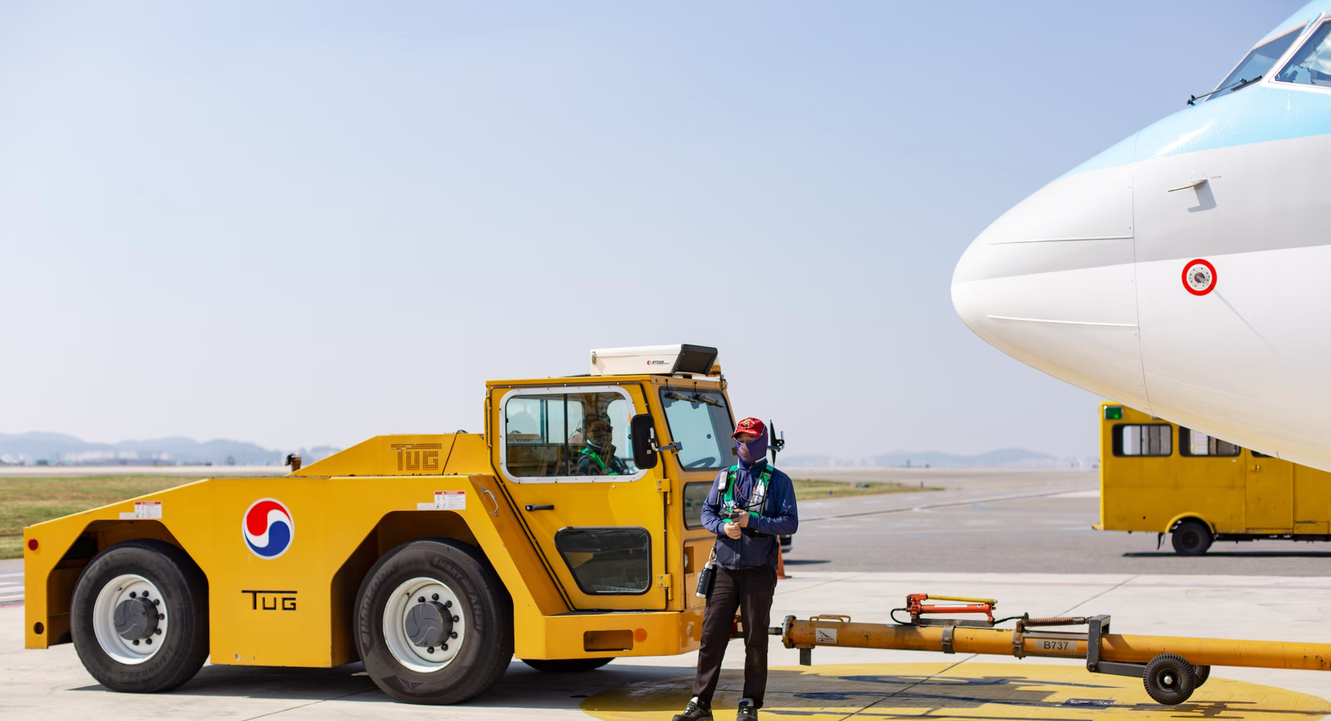 Zdjęcie przedstawia pojazd, do którego dolnej tylnej części zamontowana jest długa metalowa belka. Jest ona podpięta drugim końcem do koła samolotu. Belka, z racji swojej długości, opiera się również na małych kołach zamontowanych w jej spodniej części parzyście.