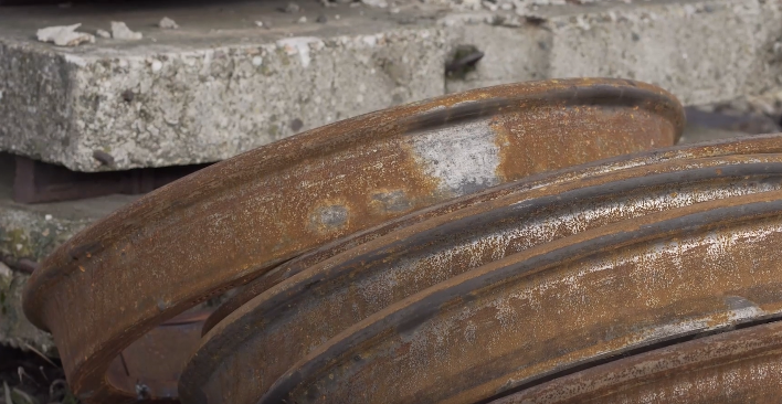 Zdjęcie przedstawia płaskie miejsce. Widoczna jest obręcz koła na której powstała usterka w postaci przetartego płaskiego miejsca. Obręcz leży na boku oparta o kilka innych obręczy.