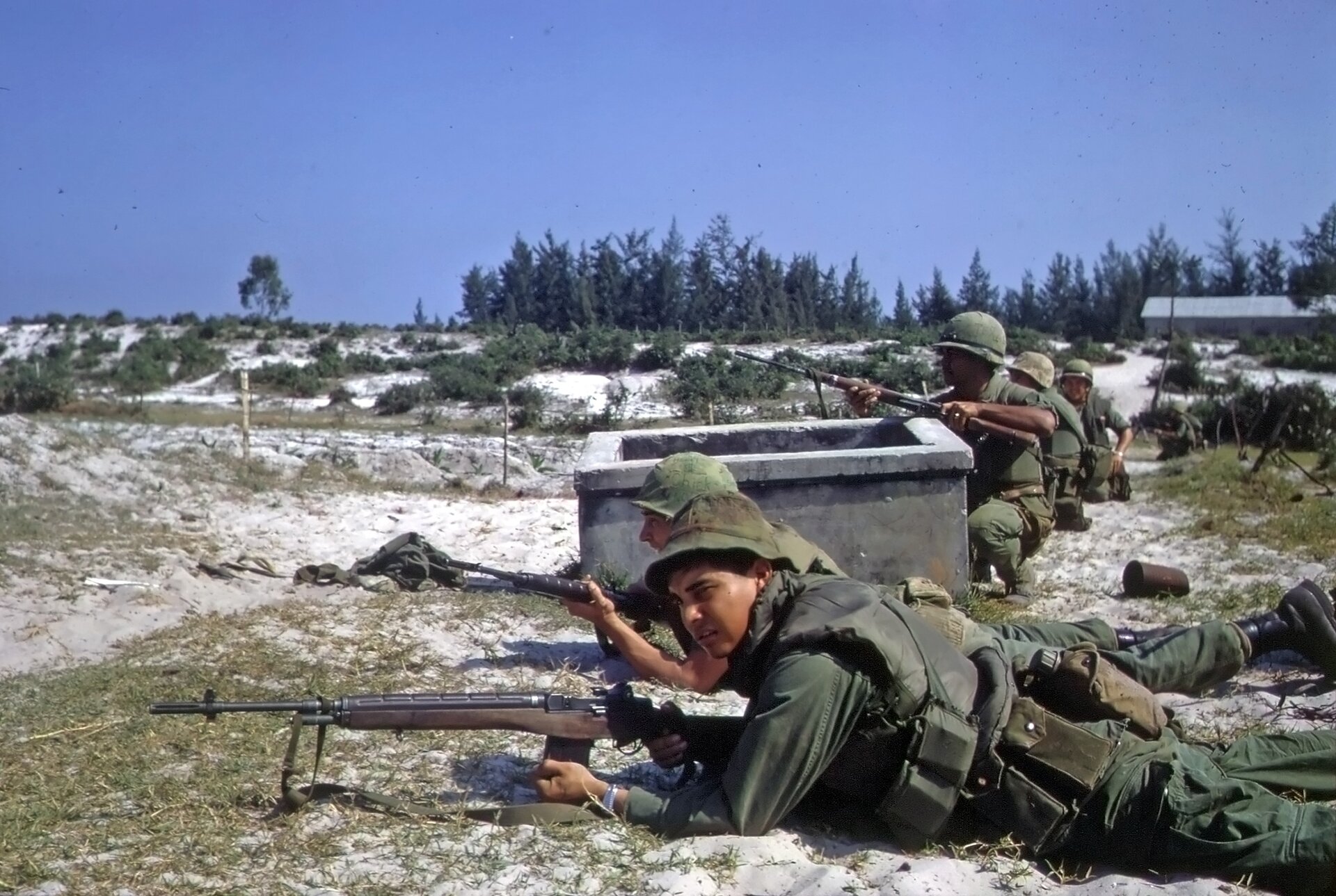 Zdjęcie ukazuje żołnierzy leżących na ziemi w szeregu. Przed nimi znajduje się broń, karabiny. 