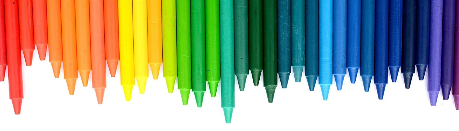 Ilustracja przedstawia zestaw kredek woskowych ułożonych od barw ciepłych do zimnych. Kredki są różnej długości i ułożone są zatemperowanymi częściami do dołu.