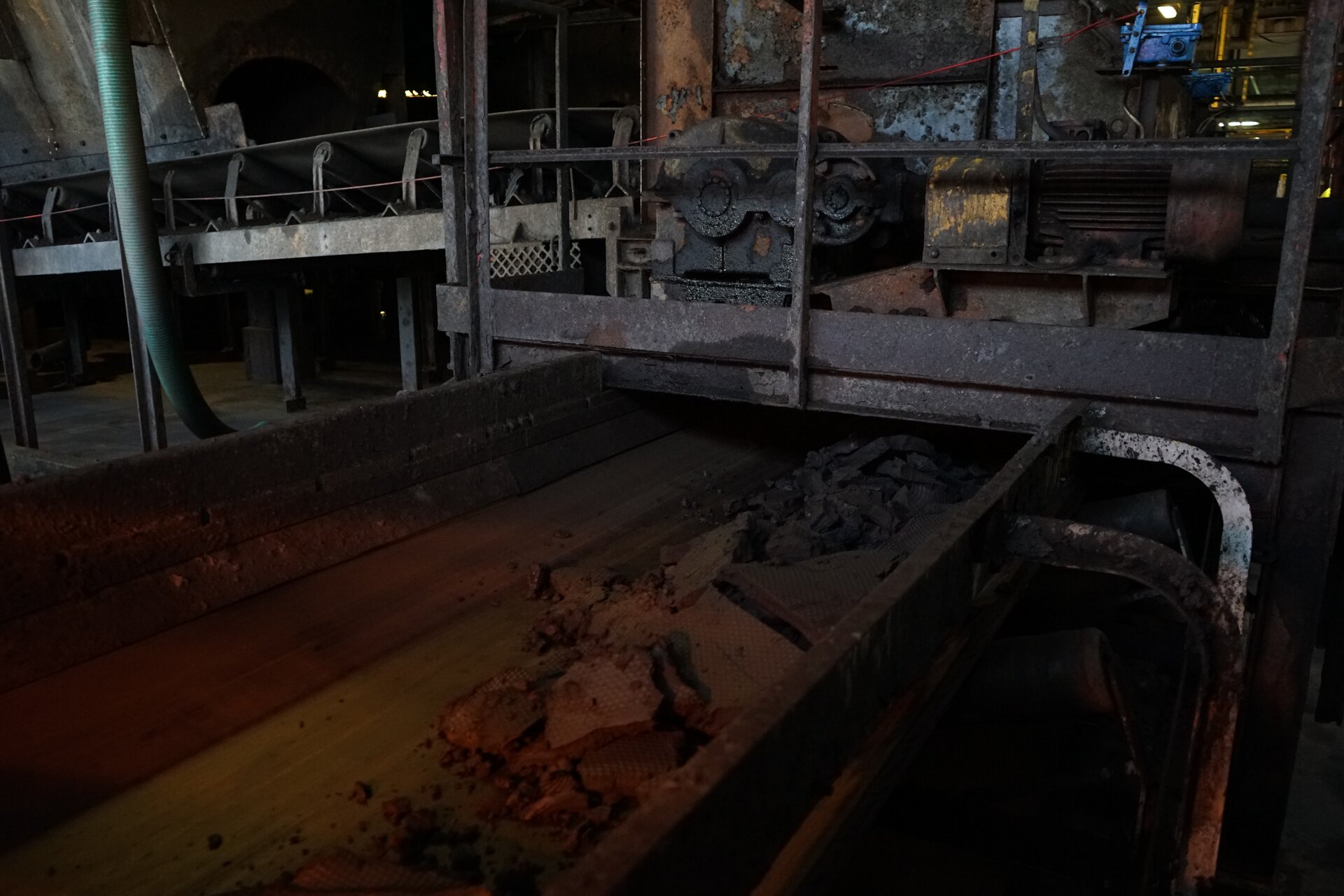 Na zdjęciu widoczny jest przenośnik taśmowy wykorzystywany do transportu materiału na większe odległości.Przenośnik jest układem modułowym. Na lekko nachylonych rolkach o kształcie walca osadzona jest taśma. Na taśmie znajduje się pokruszony urobek. Boki taśmy są zabezpieczone prostokątnymi metalowymi barierkami zabezpieczającymi urobek przed wypadnięciem z taśmy. Na górze zdjęcia widać końcówkę taśmociągu. Nad korytem osadzona jest jednostka napędowa. Taśmociąg znajduje się w budynku przemysłowym.Poniżej zdjęcia widoczny jest przycisk multimedialny z nagraniem audio. Treść nagrania jest zgodna z tytułem zdjęcia.