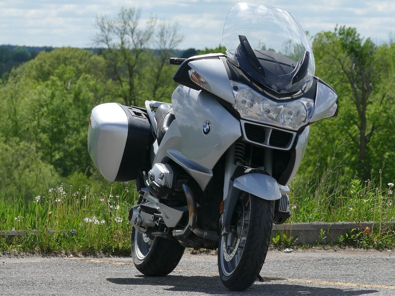 Zdjęcie przedstawia srebrny motocykl. Pojazd ma boczne bagażniki, wyższą przednią szybę. 