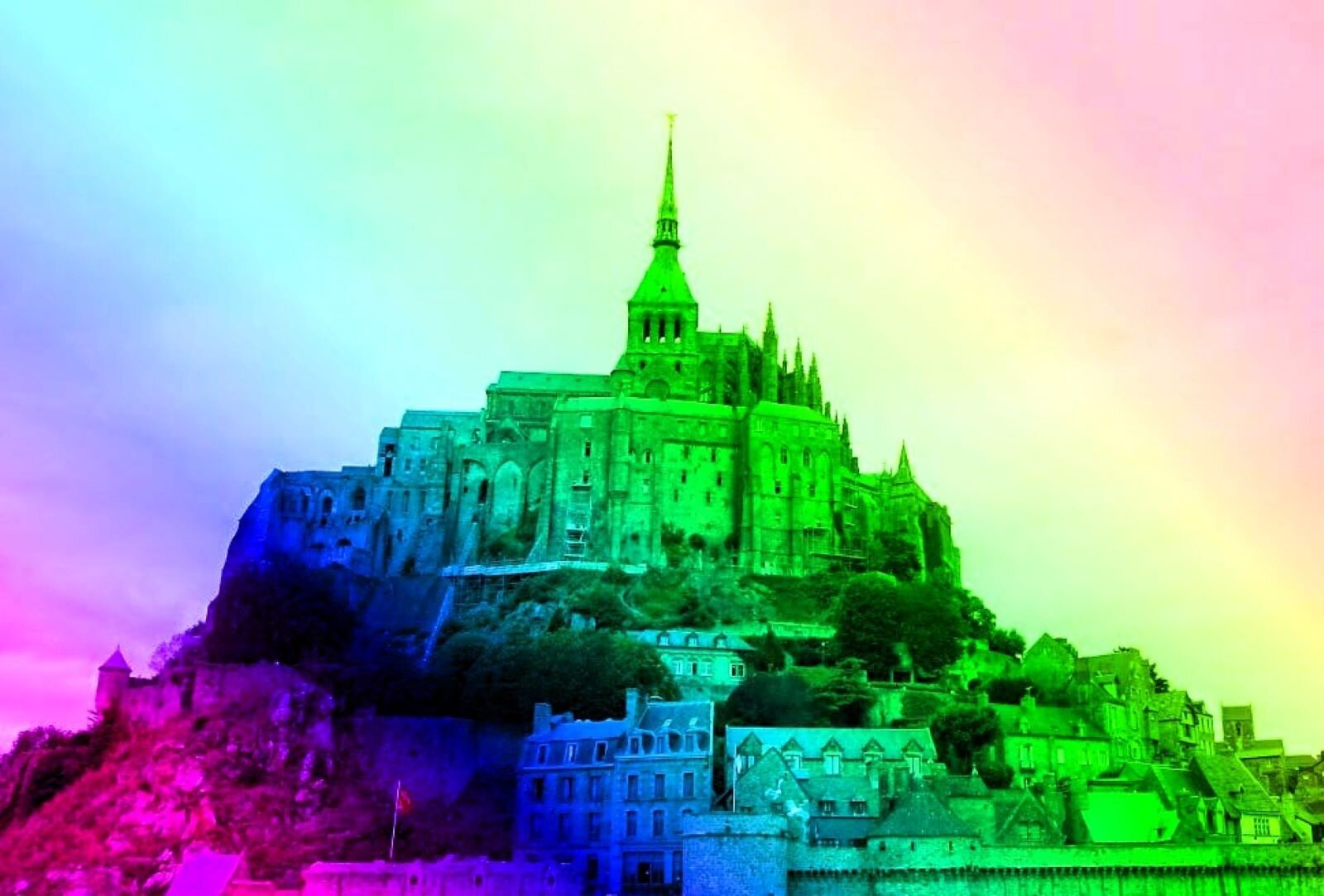 Fotografia przedstawia Wzgórze Saint Michel we Francji, wraz z zabudowaniami sanktuarium. To skalista wyspa pokryta zabudowaniami,  nad którymi góruje wieża katedry. Zdjęcie zostało edytowane przez nałożenie barwnego filtra, który pokrywa obraz przezroczystą wielobarwną powloką. 