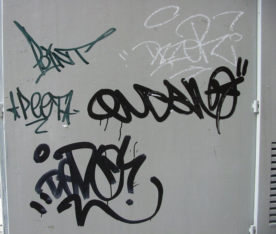 Graffiti z przykładem tagu: na szarym jednolitym tle ściany widocznych jest kilka tagów różnej wielkości. 