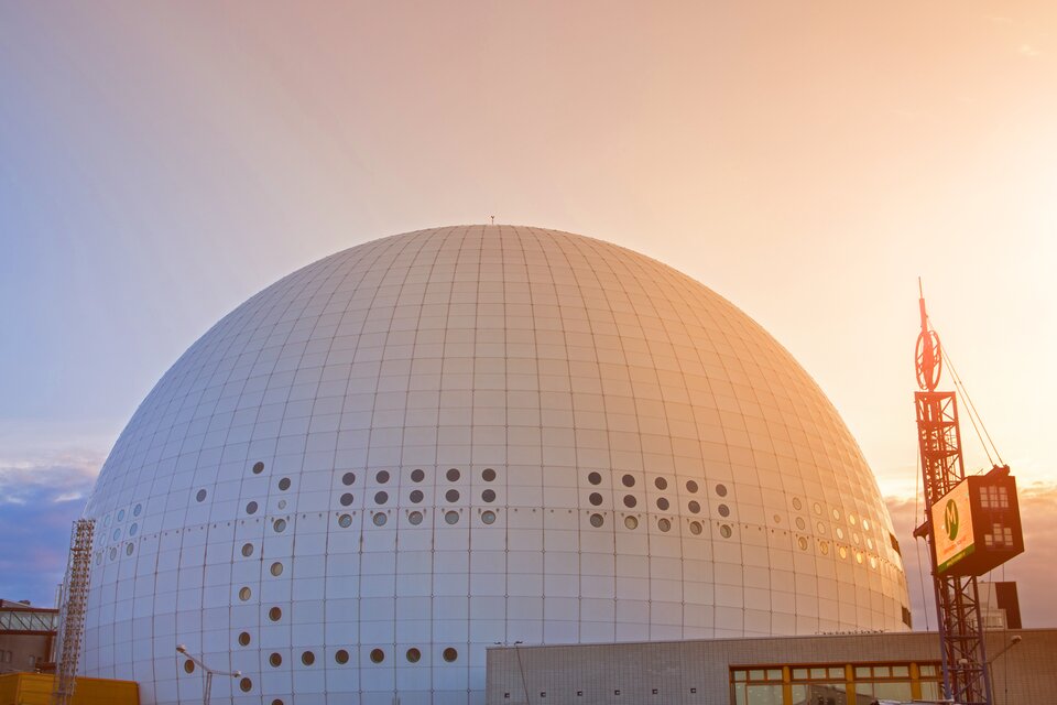 Zdjęcie przedstawiające stadion Avicii Arena w Sztokholmie. Budynek w kształcie kopuły z małymi okrągłymi oknami.