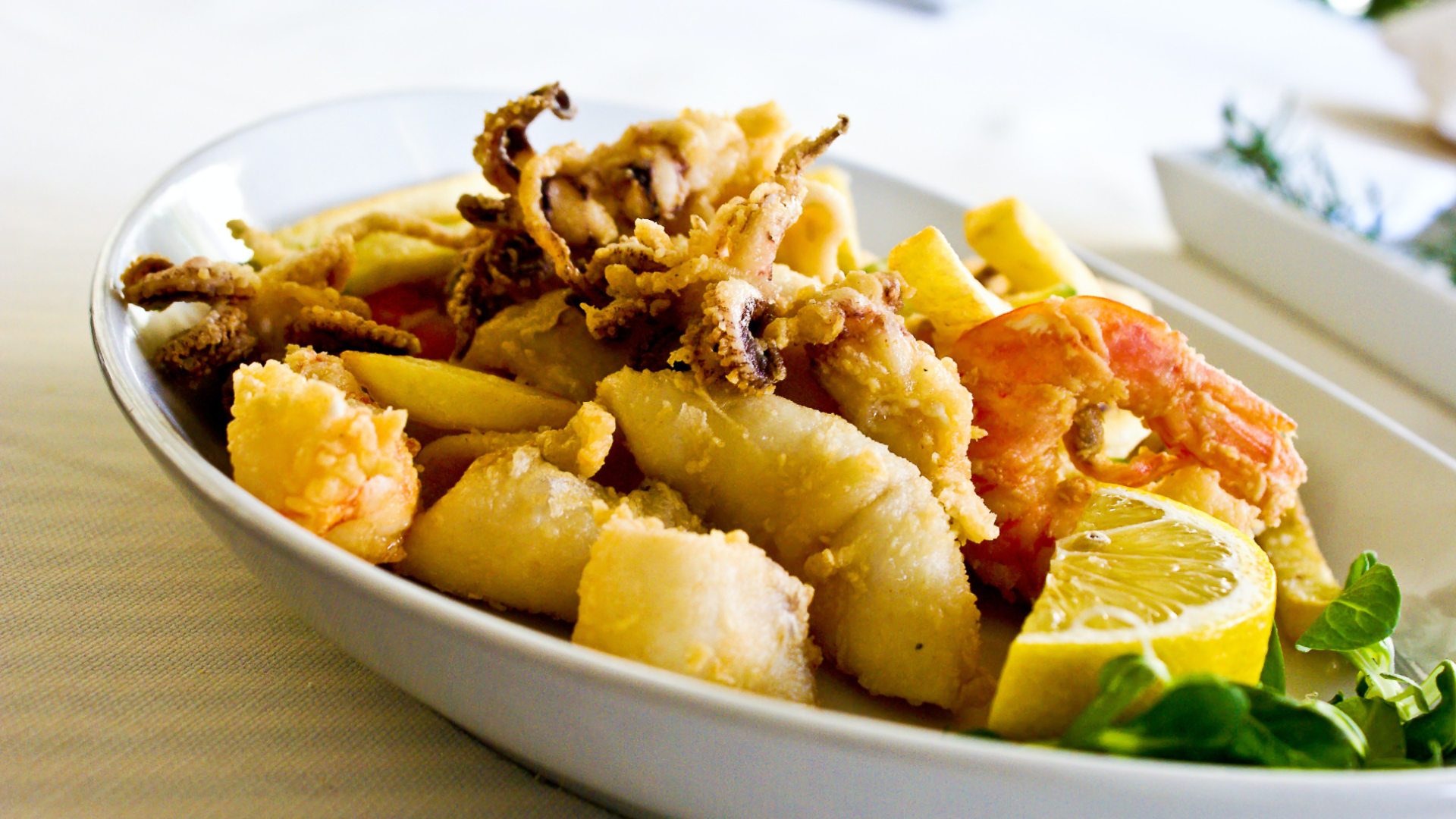 Zdjęcie przedstawia półmisek ze smażonymi owocami morza. Na półmisku znajduje się także kawałek cytryny i jakieś listki.