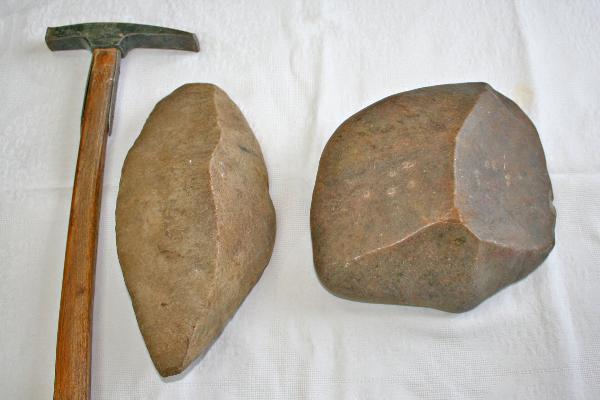 Na zdjęciu dwa graniaki. To fragmenty skał z powierzchnią wygładzoną przez wiatr i wyraźnymi krawędziami. Obok dla porównania wielkości leży młotek geologiczny. Graniaki są nieco mniejsze od młotka.