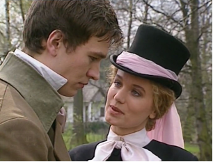 Zdjęcie przedstawia kadr z filmu. Ukazana jest młoda kobieta w eleganckiej sukni z zawiązaną pod szyją kokardą. Kobieta ma na głowie toczek przewiązany szeroką szarfą. Obok kobiety stoi odwrócony do niej swoim lewym profilem młody mężczyzna w surducie. Ma pochyloną głowę. Kobieta patrzy mężczyźnie w oczy.