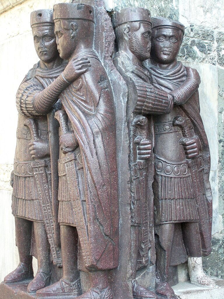 Zdjęcie przedstawia rzeźbę. Widoczni są na niej czterej władcy: dwóch augustów i dwóch władców niższej rangi z tytułem cezara. Mężczyźni stoją w parach i obejmują się ramionami.