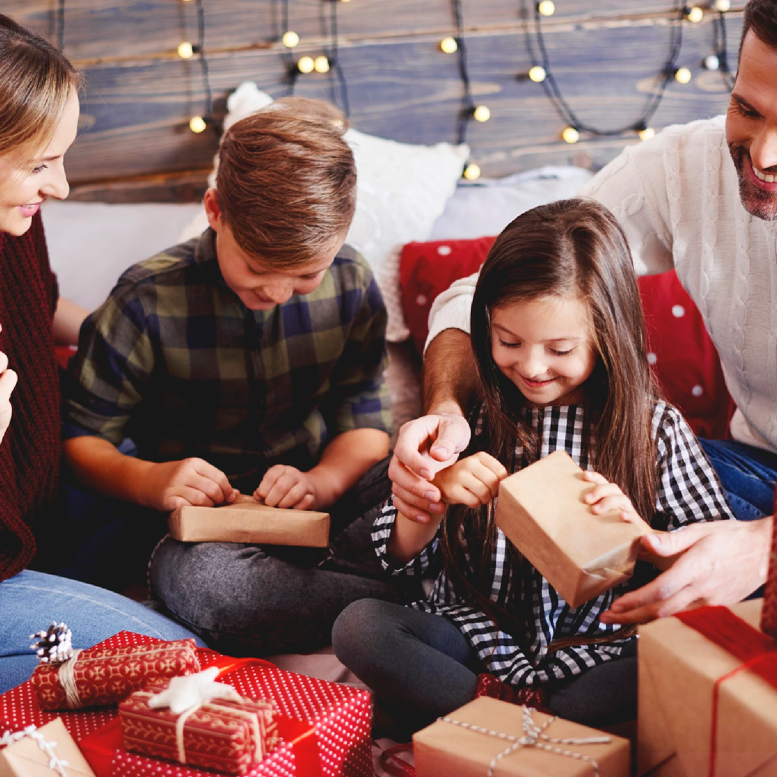 Zdjęcie przedstawia dwoje dzieci z rodzicami, które rozpakowują prezenty. 