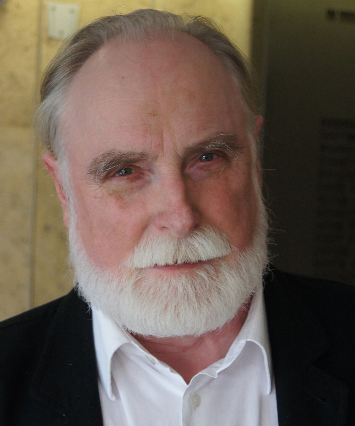 Zdjęcie przedstawia mężczyznę w sile wieku. Mężczyzna ma krótką, siwą brodę i siwiejące wąsy. Jego włosy są szpakowate, proste i krótkie. Mężczyzna ubrany jest w koszulę i marynarkę.