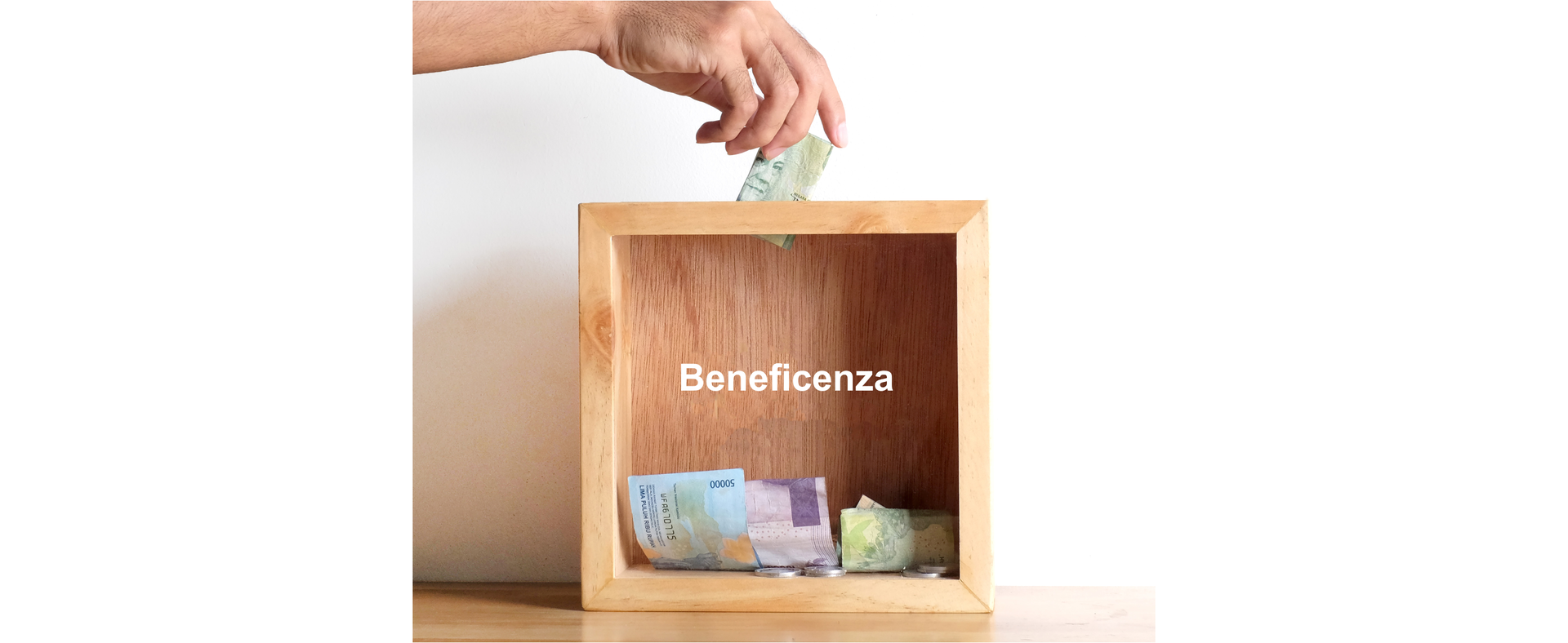 Zdjęcie przedstawia skarbonę z przezroczystym frontem. Wewnątrz znajdują się pieniądze. Widoczna jest dłoń wrzucająca banknot do skarbony. Na skarbonie znajduje się napis: Beneficenza.