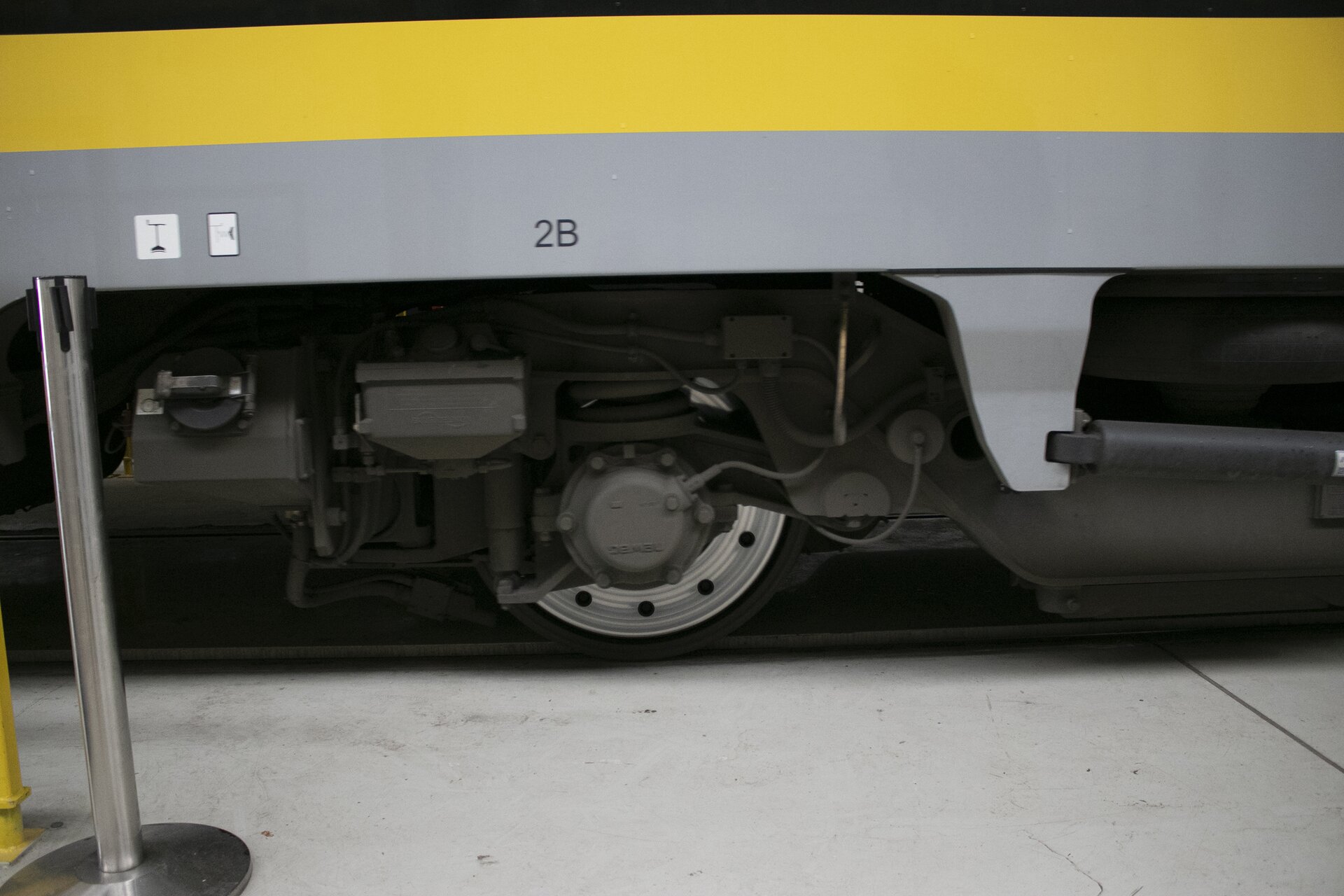 Zdjęcie przedstawia piasecznicę. Pokazany jest fragment wagonu pociągu widoczny boku. Na środku zdjęcia widać koło. Na tym zdjęciu trudniej jest zauważyć piaseczniczę. Znajduje się ona po lewej stronie widocznego na zdjęciu koła. Piasecznica znajduje się obok kół pociągu, wyglądem przypomina rurę wydechową. Służy ona do posypywania szyn piaskiem w celu zwiększenia tarcia pomiędzy kołem a szyną w celu przywrócenia utraconej przez koło przyczepności lub w celu zapobiegnięcia utracie przyczepności.