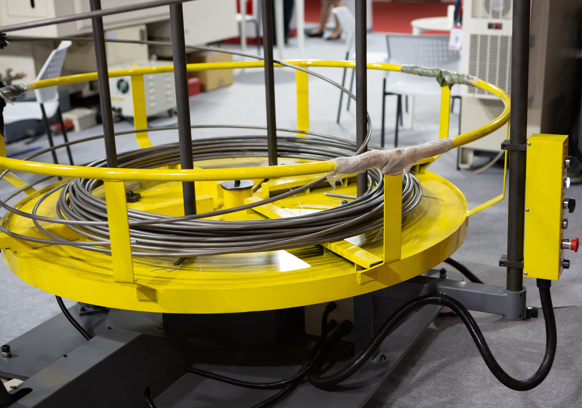 Zdjęcie przedstawia maszynę do prostowania i cięcia drutu. Urządzenie ma kolor żółty oraz okrągły kształt, w jego środku znajduje się nawinięty stalowy drut.