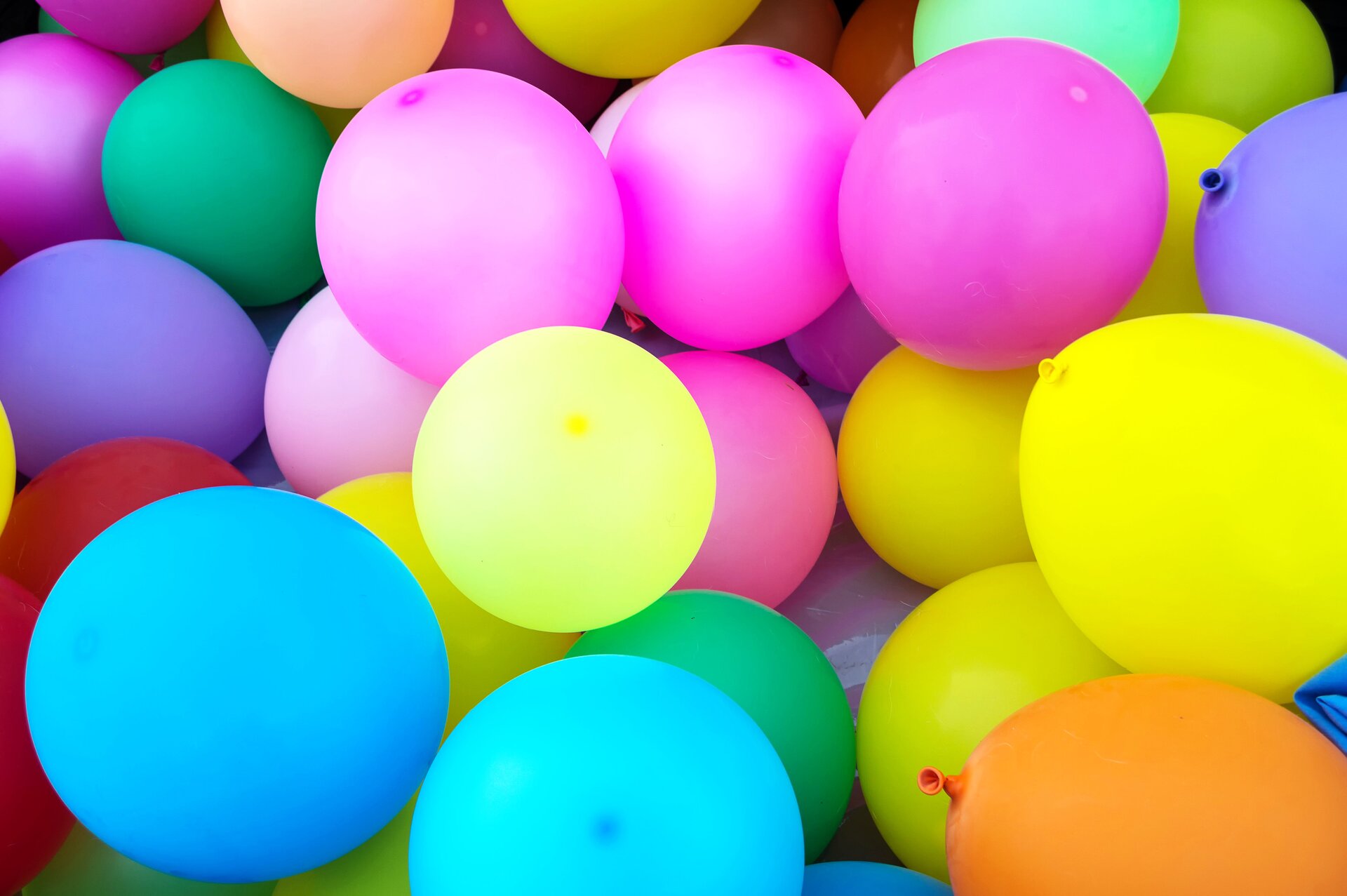 Rys. a. Zdjęcie przedstawia kompozycję złożoną z kolorowych balonów wypełnionych powietrzem. Balony są wielokolorowe, przeważają różowe, żółte, niebieskie oraz pojedyncze balony koloru zielonego i fioletowego. Pojawiają się również balony koloru czerwonego i pomarańczowego. Kompozycja jest pastelowa i radosna. 