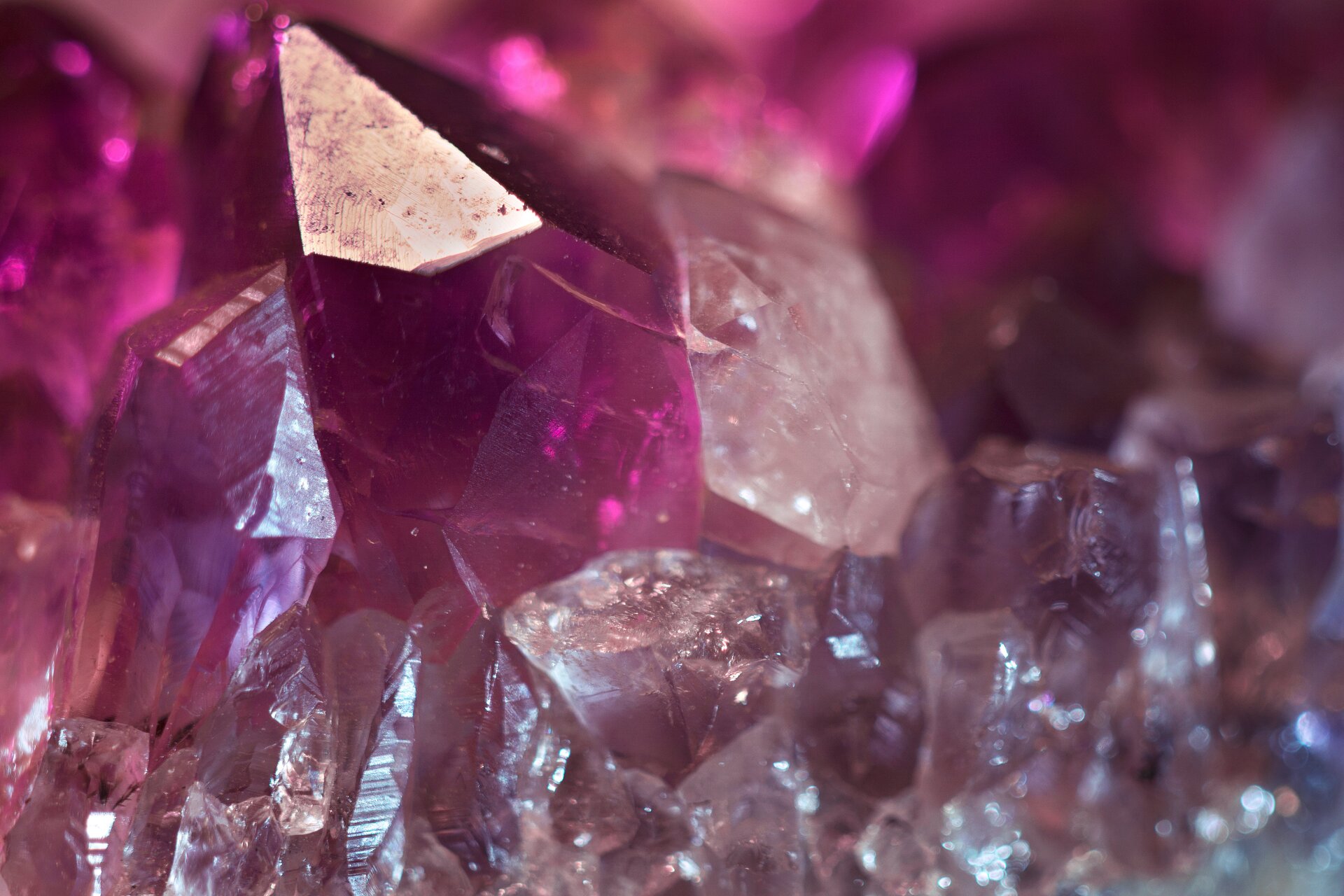 Zdjęcie przedstawia fragment kryształu ametystu w zbliżeniu, na tle pozostałej, większej części minerału. Uwagę zwracają gładkie powierzchnie krystalicznego słupka oraz intensywnie purpurowa barwa kamienia.