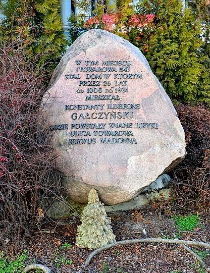 Zdjęcie przedstawia duży głaz z napisem: W tym miejscu (Towarowa 54) stał dom, w którym przez dwadzieścia pięć lat od tysiąc dziewięćset piątego roku do tysiąc dziewięćset trzydziestego pierwszego roku mieszkał Konstanty Ildefons Gałczyński, gdzie powstały znane liryki Ulica towarowa, Serwus Madonna.