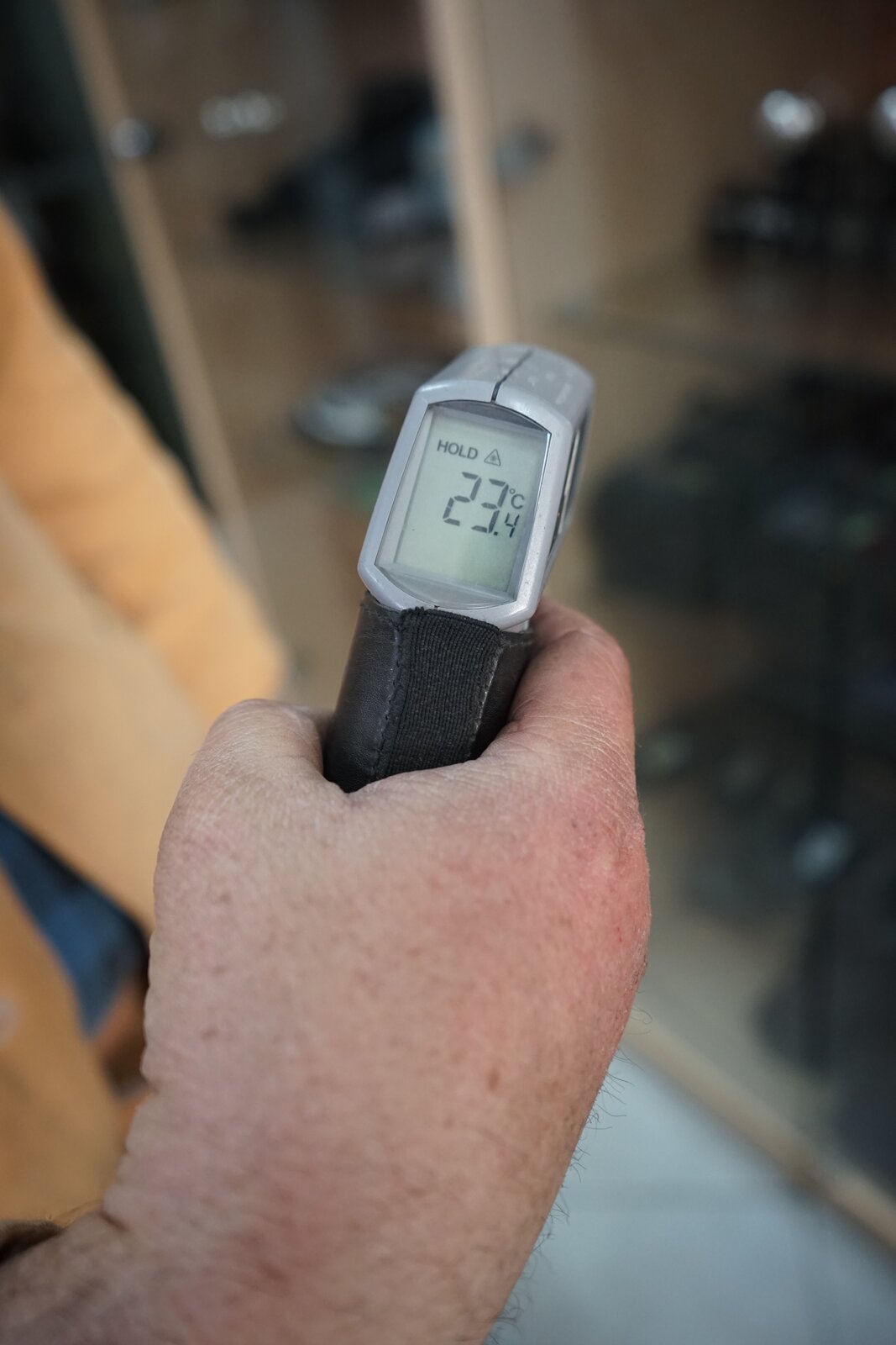 Zdjęcie przedstawia pirometr trzymany w dłoni przez górnika od strony wyświetlacza. Wyświetlacz wbudowany jest w głowicę i znajduje się od strony osoby wykonującej pomiar, powyżej uchwytu pistoletowego. Na ekranie wyświetla się temperatura dwadzieścia trzy i cztery dziesiąte stopnia Celsjusza. 