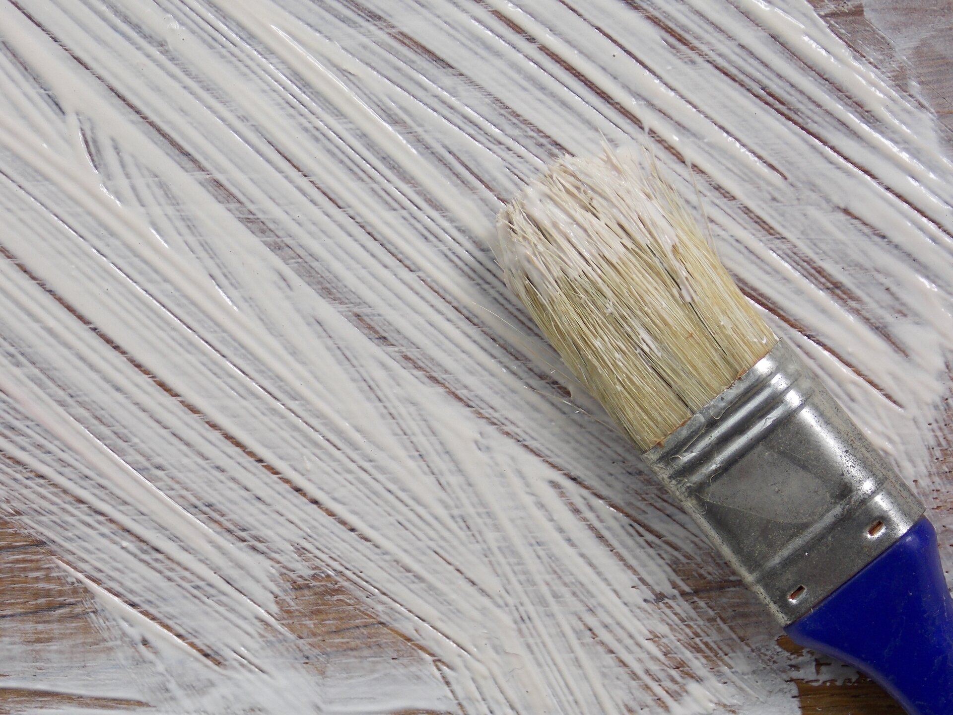 Ilustracja przedstawia pędzel z żółtym włosiem, na którego końcu znajduje się farba. Tłem jest zamalowana na biało powierzchnia z widocznymi pociągnięciami pędzla.