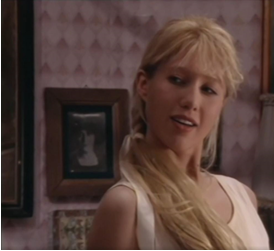 Zdjęcie przedstawia młodą kobietę. Ma długie, blond włosy, które opadają jej na prawe ramię. Ubrana jest w białą koszulkę na ramiączka. Ma lekko otwarte usta, patrzy w lewą stronę zdjęcia.