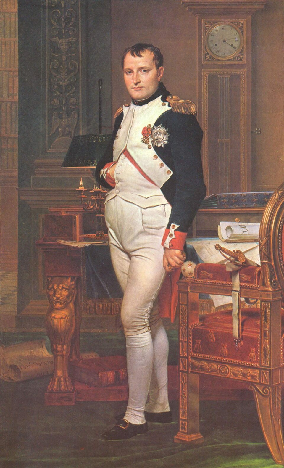 Portret mężczyzny stojącego w eleganckim wnętrzu, ukazanego w pełnej postaci. Ma krótkie, ciemne włosy, jasną cerę i spokojny, pewny siebie wyraz twarzy. Ubrany jest w charakterystyczny mundur wojskowy: białe spodnie i kamizelkę oraz ciemny, granatowy płaszcz z czerwonymi mankietami i złotymi epoletami na ramionach. Na piersi widoczne są odznaczenia. Postać stoi w swobodnej, ale zdecydowanej pozie — jedna ręka wsunięta jest za połę munduru, druga opiera się na meblu. Obok znajduje się bogato zdobione krzesło, na którym leży miecz oraz zwój papieru. W tle widoczny jest zegar stojący, biurko z dokumentami i świecami oraz regał z książkami. Wnętrze jest urządzone w stylu klasycystycznym, z ciepłą kolorystyką i starannie oddanymi detalami. Obraz przedstawia Napoleona Bonaparte w jego gabinecie.