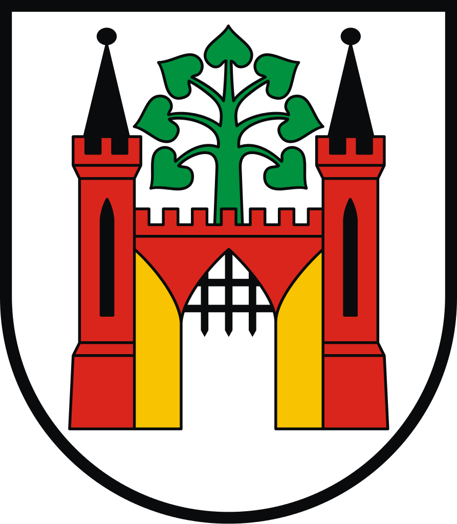 Kliknij, aby powiększyć. Kolorowa grafika przedstawia herb miasta Lipna. W centrum widnieje czerwona brama z dwiema wieżami i otwartymi złotymi wrotami oraz częściowo podniesioną kratą. Na murze łączącym dwie wieże jest zielone drzewo - lipa. Tło jest białe.