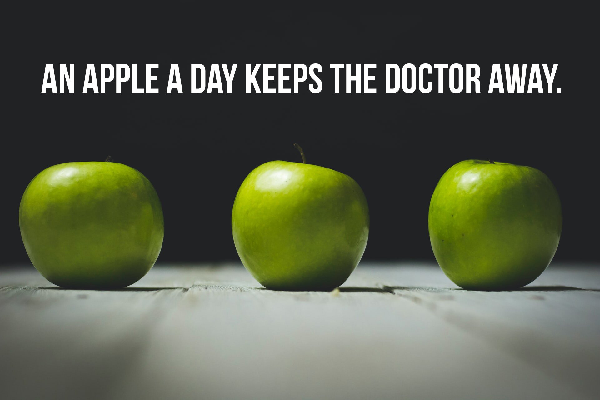 Grafika ukazuje trzy zielone jabłka, nad którymi widoczny jest napis w języku angielskim: AN APPLE A DAY KEEPS THE DOCTOR AWAY.