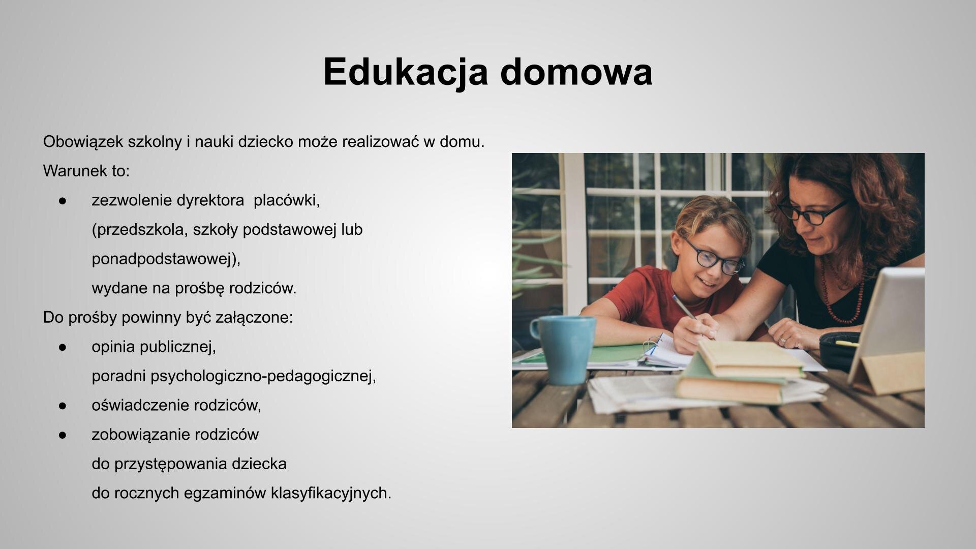 Slajd zatytułowany: Edukacja domowa. Tekst na slajdzie: Obowiązek szkolny i nauki dziecko może realizować w domu. Warunek to: zezwolenie dyrektora  placówki (przedszkola, szkoły podstawowej lub ponadpodstawowej) wydane na prośbę rodziców.  Do prośby powinny być załączone:  opinia publicznej poradni psychologiczno‑pedagogicznej,  oświadczenie rodziców, zobowiązanie rodziców do przystępowania dziecka do rocznych egzaminów klasyfikacyjnych. Po prawej stronie slajdu widoczne jest zdjęcie przedstawiające chłopca w okularach siedzącego przy stole, patrzącego na kartki umieszczone w segregatorze. Po jego lewej stronie siedzi kobieta w okularach. W prawej dłoni trzyma długopis, lewą dłoń opiera na notesie. Na stoliku widać dwie książki i niebieski kubek.