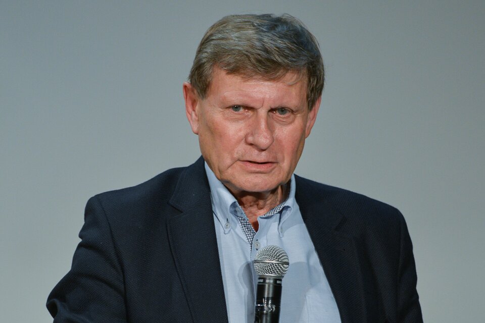 Zdjęcie przedstawia mężczyznę średnim wieku. Ma krótkie, gęste, szpakowate włosy, zaczesane w prawo. Ubrany jest w koszulę i marynarkę. Mówi do mikrofonu.