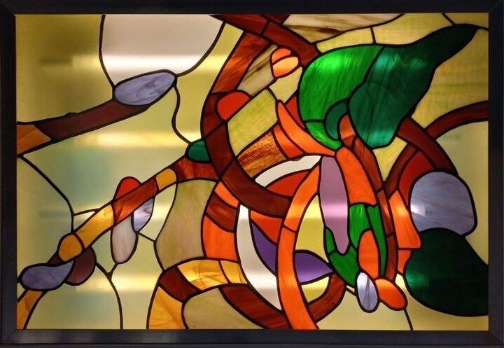 Zdęcie przedstawia współczesny witraż, wykonany przez Iwonę Werpachowską. To kompozycja asymetryczna składająca się z łodyg i liści oraz pąków kwiatów. Łodygi są poplątane, ciężar kompozycji przechyla się na prawą stronę.