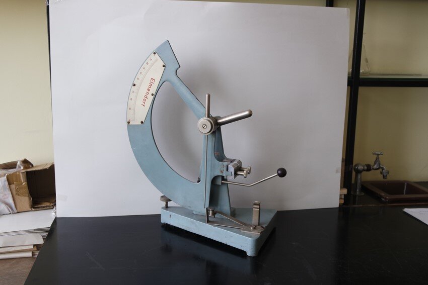 Zdjęcie przedstawia aparat Elmendorfa do oznaczania oporu przedarcia. Szczegółowy opis wyglądu urządzenia znajduje się w podpisie grafiki. 