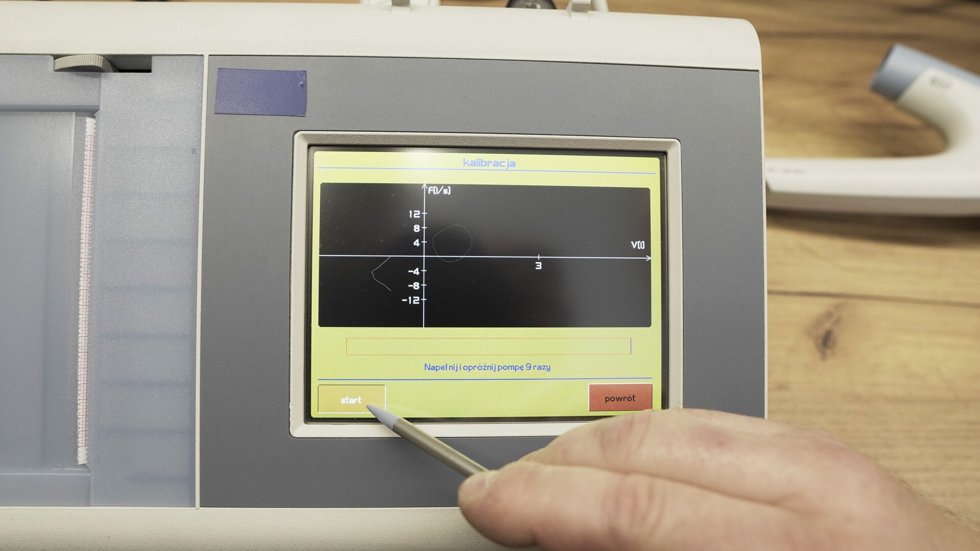 Na zdjęciu pokazano przybliżenie ekranu spirometru. Technik wybiera na klawiaturze ekranowej przycisk Start.